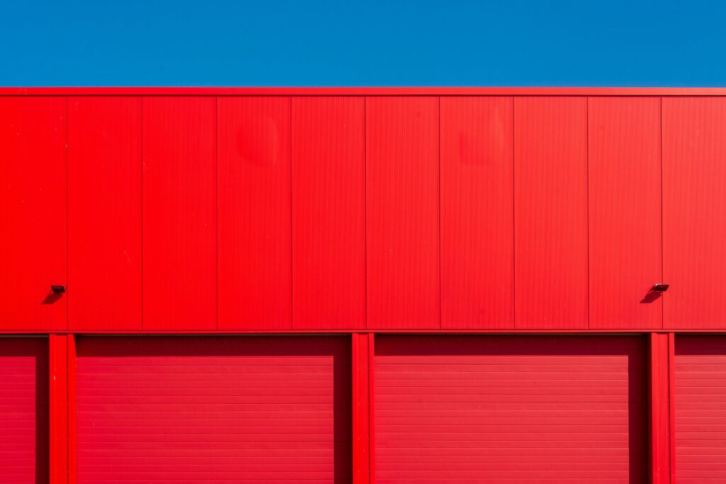 Home Bright red garage doors of an industrial building against a clear blue sky, showcasing minimalism.